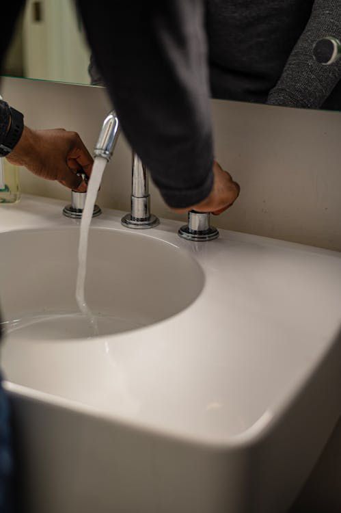Person's hand turns on a silver faucet to check water drainage.